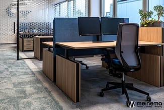 Kantoorinrichting met houten bureaus, blauwe akoestische schermen, zwarte bureaustoel en potplanten in modern kantoorruimte.