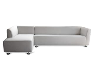 Grijze hoekbank met chaise longue links, chromen poten, modern design op witte achtergrond.
