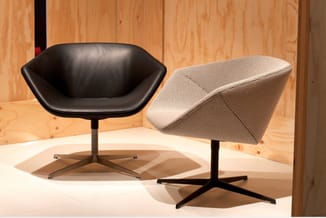 Twee moderne fauteuils met zwart metalen voet: één zwart lederen uitvoering en één in beige stof, in houten interieur.