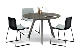 Ronde grijze tafel met grijs gestoffeerde stoel en twee zwarte stoelen met lichtblauwe zitting, vases en glazen op tafel.