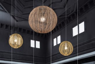 Drie hangende rieten bollen in natuurlijke en goudkleurige tinten in een zwarte ruimte met ornamentale plafonddetails.