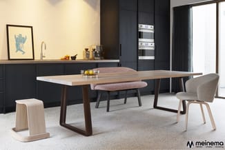 Moderne keuken en eetkamer met houten eettafel, donkerbruine poten, beige stoelen en houten krukje. Zwarte keukenkasten met i