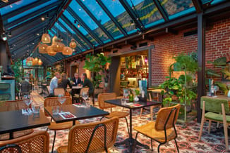 Modern kantoor met glazen overkapping, rieten stoelen, zwarte tafels, bakstenen wanden, hangende gouden lampen en groene plan