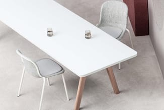 Witte rechthoekige vergadertafel met houten poten, twee grijze stoelen met witte frame, twee waterglazen op tafel, beige vloe