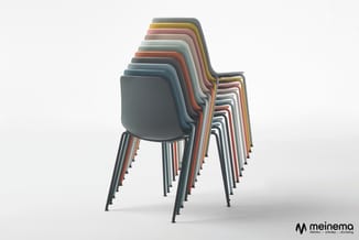 Gestapelde kunststof stoelen in verschillende kleuren (grijs, geel, roze, rood, wit, zwart) met metalen poten tegen lichte ac