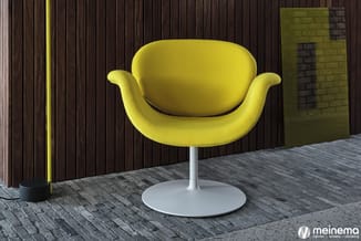 Gele fauteuil met ergonomische schaalvorm op wit voetsteun, tegen donkerbruine houten lamelbekleding, naast gele verlichtings