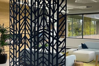 Zwart metalen scheidingswand met geometrisch patroon in modern kantoorinterieur, naast grijze zitbank en houten elementen.