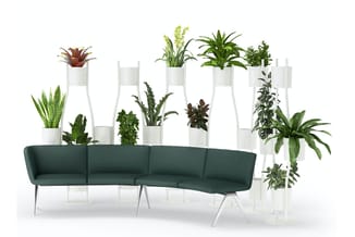 Grijsgroene gebogen bank met metalen poten voor kantoorruimte, achter witte plantenstelling met diverse potplanten.