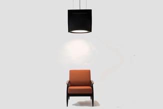 Oranje fauteuil met zwart houten frame onder zwarte hangende plafondlamp in minimalistisch interieur.
