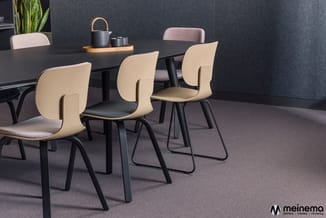 Moderne vergaderruimte met zwarte tafel, crèmekleurige stoelen met zwarte poten, grijze wand en tafelaccesoires.