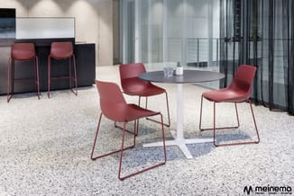 Rond tafel met grijs blad en wit onderstel, omgeven door vier bordeauxrode stoelen met metalen frame in moderne kantoorruimte