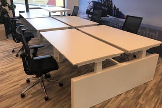 Modern kantoor met lichte houten vergadertafel, zwarte ergonomische bureaustoelen, monitors en houten vloer.