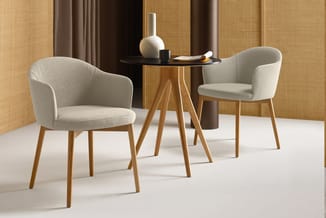 Twee grijze stoelen met houten poten rond een kleine ronde tafel met zwart blad in een kantooromgeving met houten wanden.