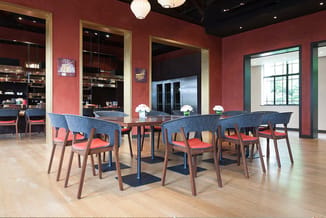 Moderne vergaderruimte met lange tafel, blauwe stoelen met rode zitting, rode wanden, houten vloer en raampartijen.