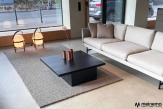 Moderne loungeruimte met lichtgrijze hoekbank, zwart lage vierkante tafel, grijze tapijten, houten vloer en twee decoratieve