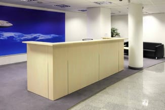 Moderne receptiebalie in licht hout met grijze werkblad in kantoorruimte met blauwe wanddecoratie en zuilen.