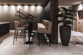 Moderne kantoorruimte met zwarte vleugel, twee beige barstoeien, zwarte bartafel, grote donkergrijze plant in pot en grijze t