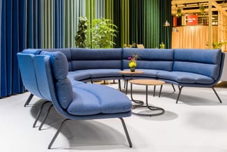 Blauwe loungezetel en grijsblauwe hoekbank in moderne kantoorruimte met groene verticale lamellen, houten tafels en potplante