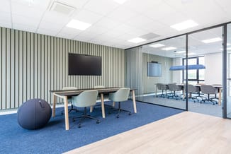 Modern kantoor met verticaal gerande wanden in groen-grijs, vergadertafel met lichtgroene stoelen, blauwe zitbal, TV-scherm e