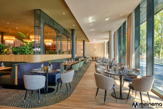 Modern restaurant met groene boxen, beige stoelen, houten tafels, groot raamoppervlak en geïntegreerde verlichting.