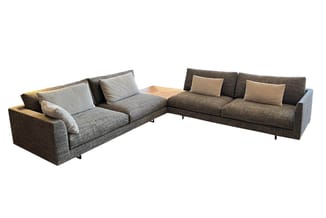 Hoekbank in grijsbruin geweven stof met beige kussens, twee zitdelen met houten accent, op wit geïsoleerde achtergrond.