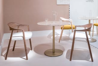 Ronde marmeren tafel met gouden voet, omringd door houten stoelen met witte zitting in minimalistisch interieur met roze muur