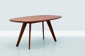 Ovale houten vergadertafel met donkerbruin fineer en vier schuine houten poten, staand in lichte ruimte.