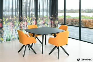 Zwarte vierkante vergadertafel met vier oranje stoelen met zwarte poten in moderne kantoorruimte met grote ramen en uitzicht