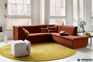 Rood-oranje hoekbank met textielbekleding in moderne woonkamer met gele rond tapijt, witte poef en grote ramen.