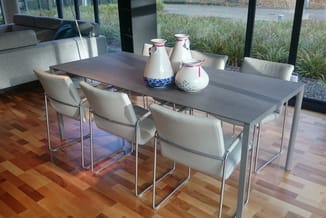 Grijze vergadertafel met vier crèmekleurige stoelen, decoratieve witte kannen, houten vloer, raampartijen met uitzicht.