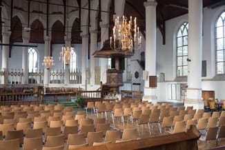 Houten stoelen met metalen poten in rijen opgesteld in een kerkinterieur met houten preekstoel, kroonluchters en grote ramen.