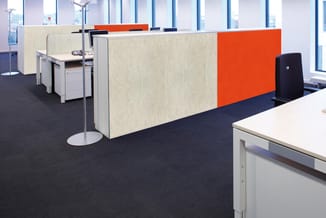 Kantoorruimte met beige akoestische schermen, oranje paneel, wit bureau, zwarte stoel en raam met uitzicht.