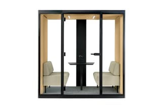 Akoestische belcel met zwart frame en houten binnenwanden, voorzien van twee beige stoelen, zwarte tafel en videocall-scherm.