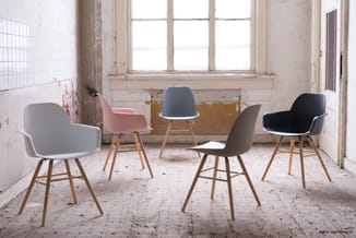 Vijf moderne stoelen met kunststof zittingen in grijs, roze, blauw, taupe en zwart met houten poten, in cirkelformatie in een