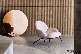 Moderne loungeinrichting met witte gestoffeerde fauteuil op zwart metalen onderstel en ronde houten spiegel tegen geribde gri