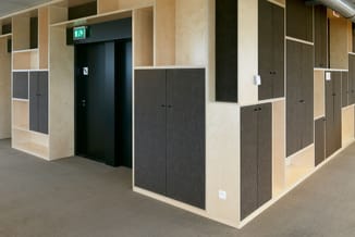 Modulaire kantoorwanden in licht hout en donkergrijs stof met gesloten kasten, open vakken en zwarte deur met nooduitgang.
