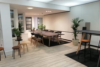 Moderne kantoorruimte met zwarte vergadertafel, houten stoelen, groene planten, witte wanden en laminaatvoer.