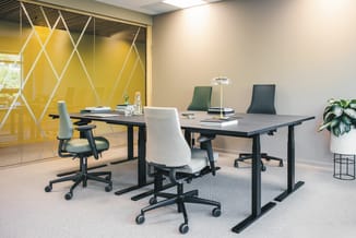 Modern kantoor met zwarte elektrisch verstelbare vergadertafel, grijze en groene ergonomische bureaustoelen, gele glazen wand