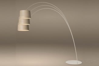 Booglamp met witte/crème metallic voet en gebogen arm met drie gestapelde cilindervormige linnen kapjes, staand in neutrale r