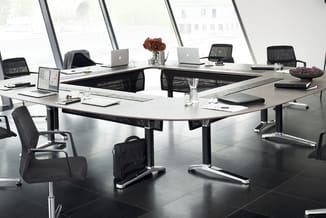 Moderne vergaderkamer met U-vormige witte vergadertafel, zwarte mesh-stoelen, laptops, glazen waterkannen en rood boeket. Gro