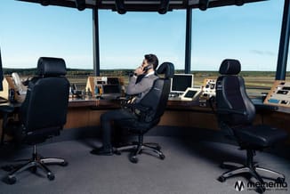 Man aan bureau in moderne toren met panoramisch uitzicht, zwarte ergonomische bureaustoel, houten werkblad met monitors en ka