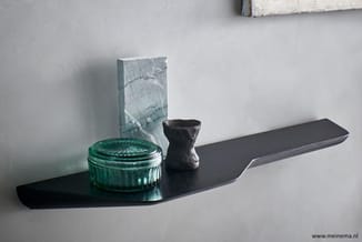 Zwarte wandplank met groene glazen doos, grijs-blauwe decoratieve blok en zwart object erop.