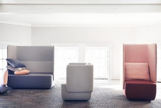 Drie modulaire loungebanken in grijs, beige en terracotta met hoge ruggen in een lichte kantoorruimte met raam.