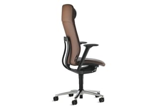 Bruine ergonomische bureaustoel met zwart frame, verstelbare armleuningen en aluminium voetsteun op wieltjes, tegen witte ach