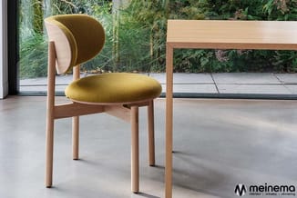 Houten stoel met geel-groen gestoffeerde zitting en gebogende bruine rugleuning, in moderne lichte ruimte met glazen wand en