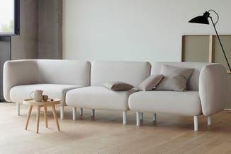 Modulaire bank in crème met afgeronde vormen, witte poten, hoekopstelling in minimalistisch interieur met houten tafel en zwa