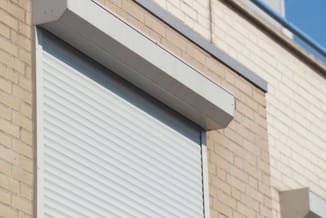 Witte aluminium jaloeziën in raamopening van bakstenen gevel met grijze kozijnlijsten.