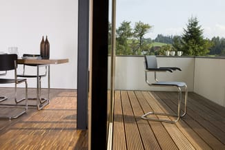 Kantoorruimte met glazen wand, zwarte stoel met armleuningen op houten terras, bruine ronde tafel en witte koffiemokken, uitz