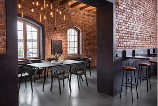 Moderne kantoorrruimte met bakstenen muren, zwarte vergadertafel, zwarte stoelen, bartafel met houten zitting, hanglamp, beto