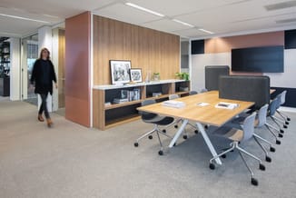 Modern kantoor met houten vergadertafel, grijze ergonomische stoelen, houten kasten met zwarte vakken, roze/rode wandpanelen